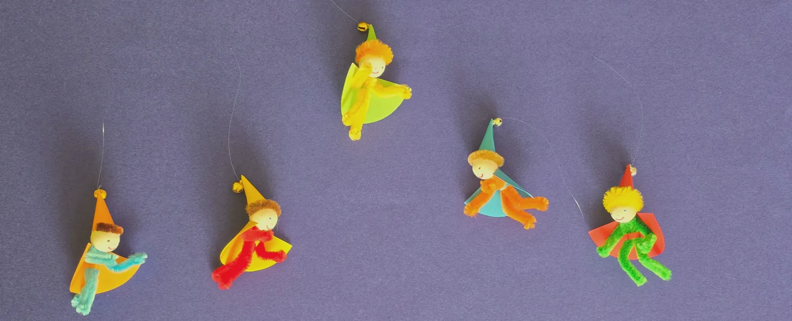 Composition d'un mobile en cours : cinq personnages colorés disposés sur un fond violet avant assemblage, pour trouver leur place et leur harmonie