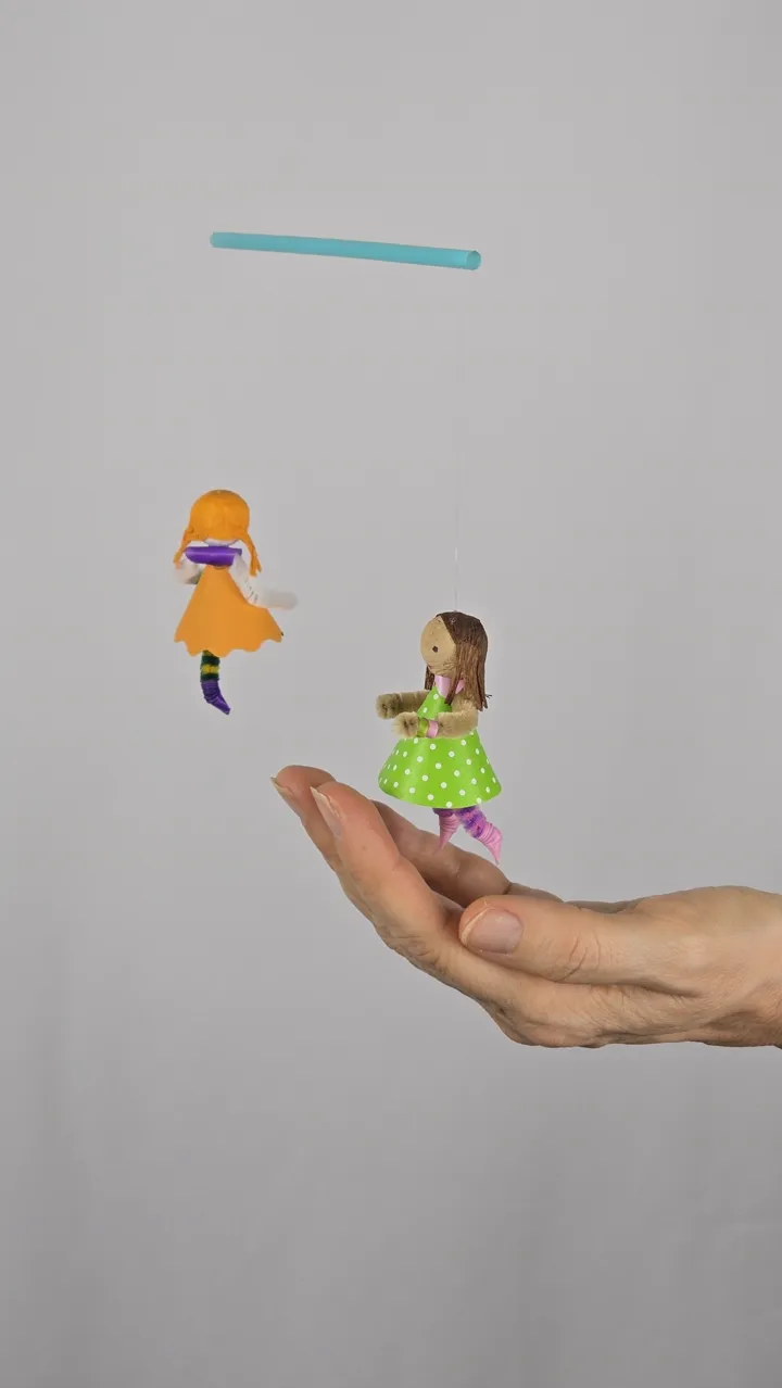 Mobile de petites coquettes - main de Clotilde tenant une fillette à robe verte